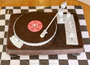 A cake in the shape of a turntable with the Self Help Radio logo on the label of the record