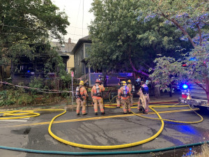 Image description: A group of Portland firefighters standing in the street outside the house on Stark street that was burned badly in a fire.